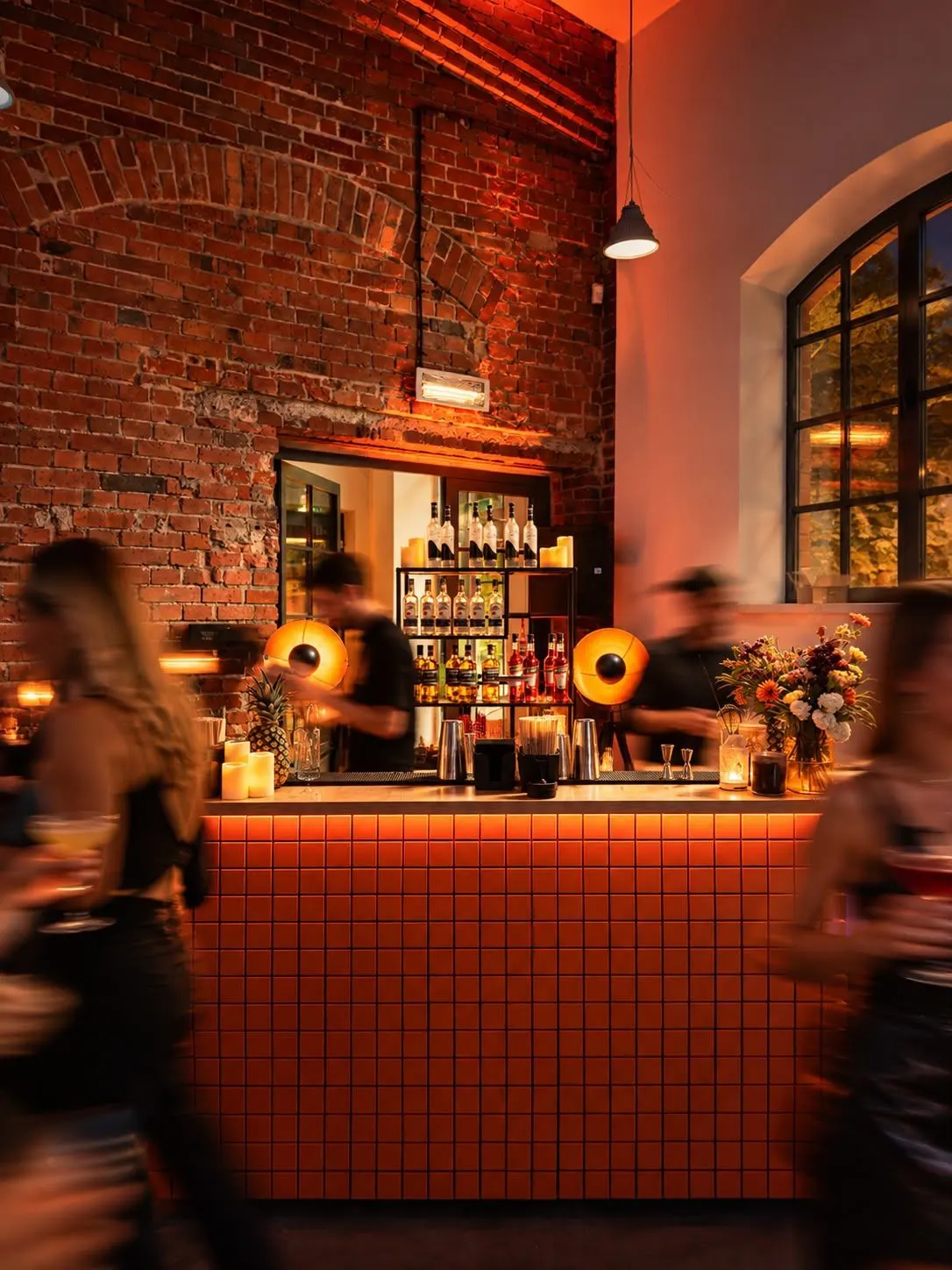 Barmani LateNightCocktailClub przy barze z czerwonych płytek, goście w ruchu